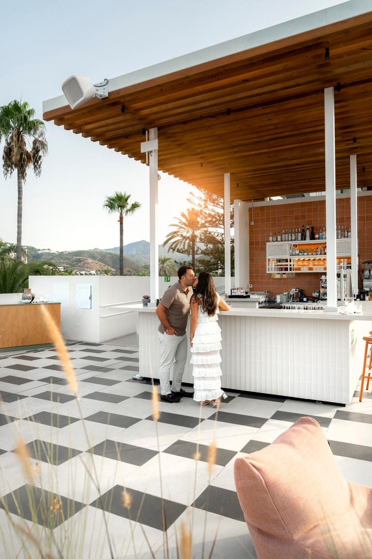 Couple kissing at a rooftop bar with hills behind
