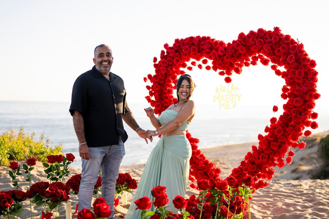 Couple holding hands and laughing beside the rose heart, roses lining the sand