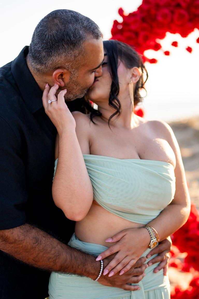 Couple kissing moments after the proposal, red roses behind them